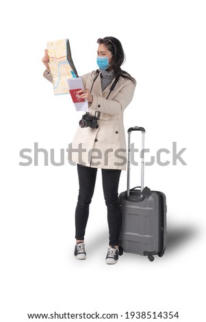 Young beautiful Asian woman holding a map and passport and wearing a medical face mask beside a Suitcase on a white isolated background, Concept of traveler tourist and vacation.