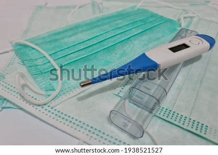 Three-layer medical mask and thermometer are starter kit during a pandemic to prevent the spread of the virus