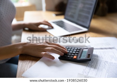 Close up young woman using calculator and laptop, checking financial documents, siting at table with papers, managing planning budget, accounting expenses, browsing internet banking services