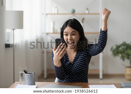 Excited young asian girl sit at desk at home triumph receive good news promotion notice on cellphone. Overjoyed Vietnamese woman feel euphoric win lottery online on smartphone. Luck concept. Royalty-Free Stock Photo #1938526612