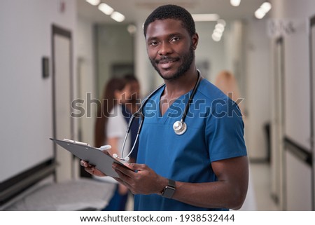 Handsome African American Doctor In Blue medical Unifrom with clipboard in hospital Royalty-Free Stock Photo #1938532444