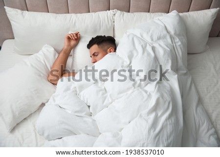 Handsome man sleeping under soft blanket in bed at home, above view Royalty-Free Stock Photo #1938537010