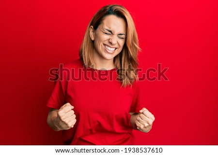 Hispanic young woman wearing casual red t shirt very happy and excited doing winner gesture with arms raised, smiling and screaming for success. celebration concept. 