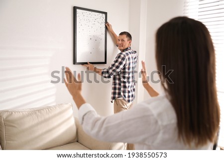 Happy couple decorating room with picture together. Interior design