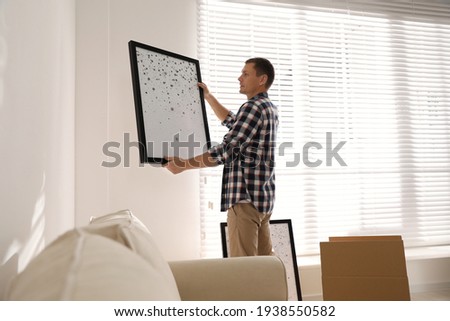 Man holding picture near white wall in room. Interior design