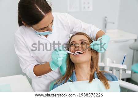 European young woman sitting in medical chair while dentist fixing her teeth at dental clinic Royalty-Free Stock Photo #1938573226