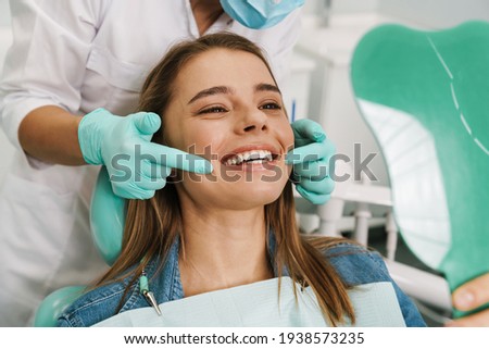 European young woman smiling while looking at mirror in dental clinic Royalty-Free Stock Photo #1938573235