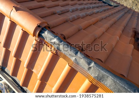 Closeup of yellow ceramic roofing ridge tiles on top of residential building roof under construction. Royalty-Free Stock Photo #1938575281