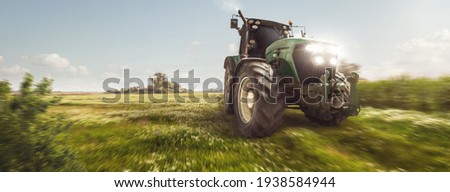 Tractor driving on a dirt road next to a field Royalty-Free Stock Photo #1938584944