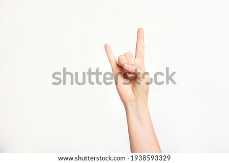 Woman's hand gesturing rock and roll, heavy metal, devil horns gesture or I love you on light grey background.