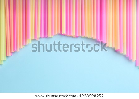 Heap of colorful plastic drinking straws on light blue background, flat lay. Space for text