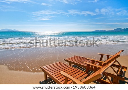 Sunbeds in front of the sea, touching the waves, on a sunny sandy beach.