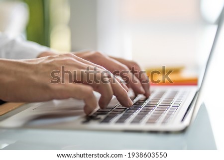 Men hand typing on computer keyboard while working from home or using internet for online shopping and social network. Laptop device and Wireless technology concept.  Royalty-Free Stock Photo #1938603550