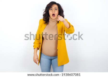 Shocked young pregnant businesswoman wearing yellow blazer over white background points front with index finger at camera and. Surprise and advertisement concept.