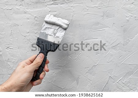 Applying putty or plaster to a vertical wall in a renovated house with a spatula or trowel. Royalty-Free Stock Photo #1938625162