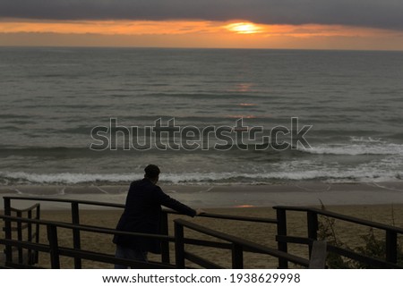 Italian boy back to back watches the sunset at the sea alone. Rear view of a young man admiring the sunset on the beach