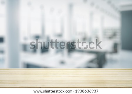 Empty wooden table top with light sunny furnished office on background, mock up