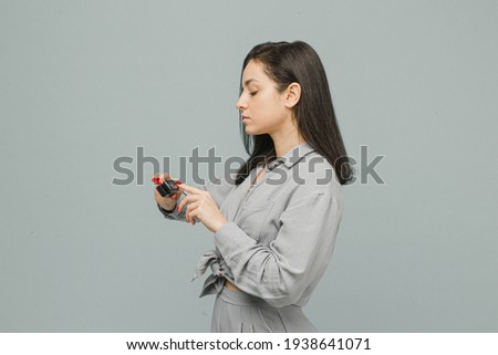 Photo female with pulse oximeter on her finger, checks her health. Wears grey dress, isolated grey color background