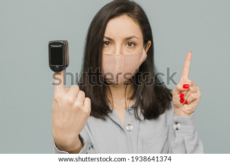 Close up photo female with pulse oximeter on her finger, checks her health. Wears grey dress, isolated grey color background