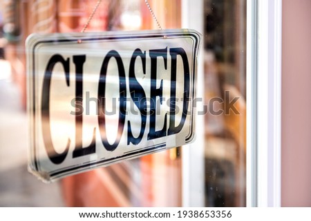 Closeup of closed white and black hanging sign on door of store retail shop business through glass window door