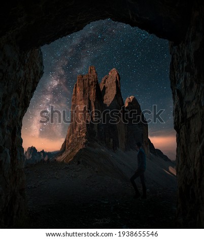 Boy, man is standing in front of moutains Tre Cime di Lavaredo in Dolomites, Italy during night with full of stars and Milky way. Amazing landscape night photo with atmosphere. 
