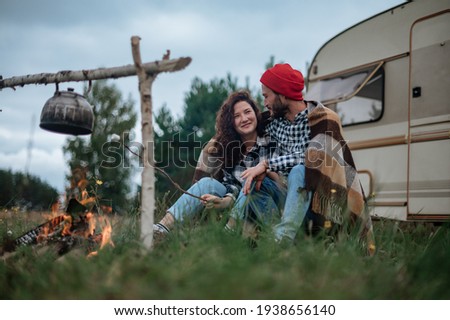 Couple in a checkered plaid roasting marshmallows on fire near the trailer home.