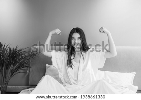 Young beautiful woman showing her biceps. A woman is doing morning exercises in the bed. sports and healthy lifestyle.