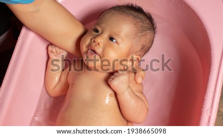 mother cleaning little baby in bathtub, baby taking a pink bath