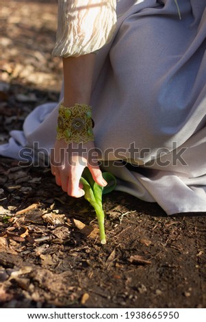 A young woman sitting on the ground touching a tulip, with a beautiful bijou cuff on her hand. Stock photography.