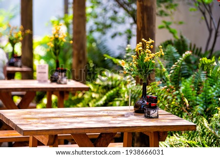 Wooden outside outdoor sitting restaurant empty area with picnic wooden tables chairs bench in patio terrace garden with green plants in Florida with flower bouquet and condiments