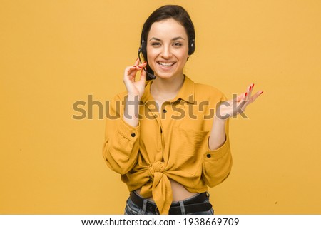 Photo of cute female with headphones and talking on microphone. Wears yellow shirt, isolated yellow color background