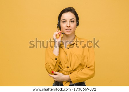 Photo of cute female with headphones and talking on microphone. Wears yellow shirt, isolated yellow color background