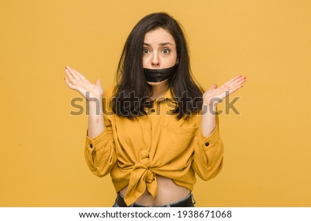 Concept photo of female victim with her mouth taped up. Wears yellow shirt, isolated yellow color background