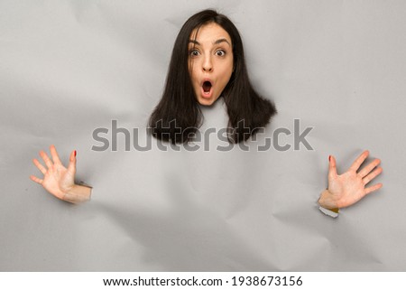 Concept photo of young female tearing paper and peeking out hole, shocked about commercial offer on copy space, isolated grey color background