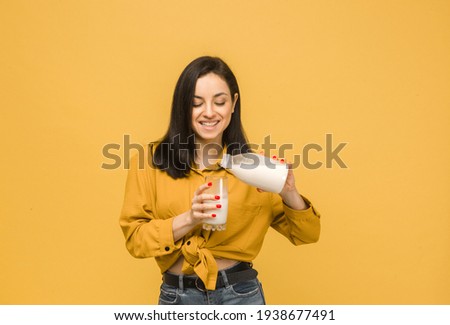 Concept photo of young female is pouring milk in glass. Wears yellow shirt, isolated yellow color background