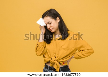 Photo of sick female has headache . Wears yellow shirt, isolated yellow color background