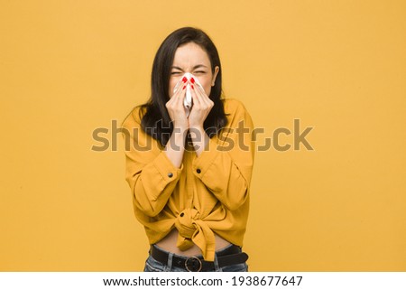 Photo of sick female is sneezing. Wears yellow shirt, isolated yellow color background