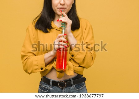 Concept photo of sweet female is drinking cocktails, summertime. Wears yellow shirt, isolated yellow color background