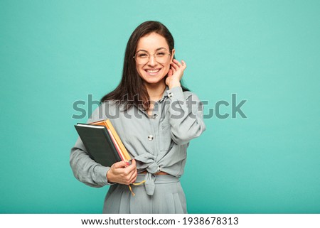 Photo of cute female holds books and smile. Wears grey shirt, isolated turquoise color background