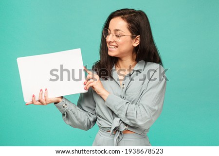 Photo of cute female in glasses holds papers. Wears grey shirt, isolated turquoise color background