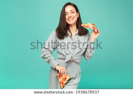 Photo of cute lady is playing with pizza, junk food. Wears grey shirt, isolated turquoise color background