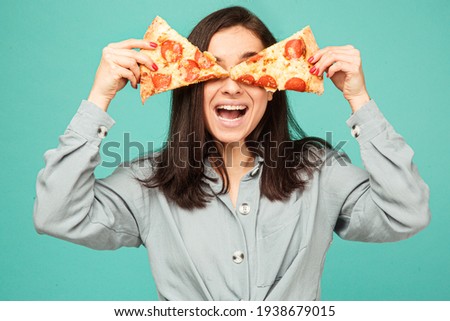 Photo of cute lady covers eyes up with pizza. Wears grey shirt, isolated turquoise color background
