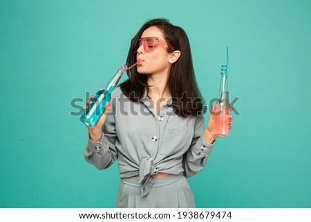 Photo of attractive lady in sunglasses drinks cocktails. Wears grey shirt, isolated turquoise color background