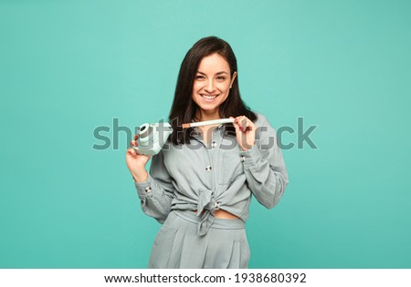 Photo of attractive lady holds camera and smiles. Wears grey shirt, isolated turquoise color background