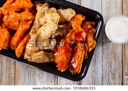 A top down view of a to-go container of assorted flavors of chicken wings.