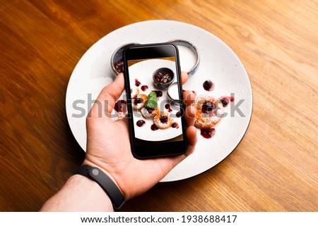 Photo of male hand photographing morning plate with pancakes with gem over wooden background.