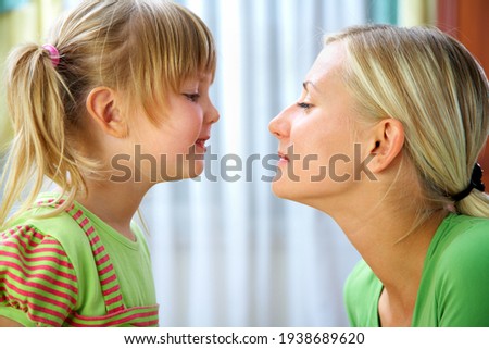 Young blonde mother gently kisses her little  daughter at home