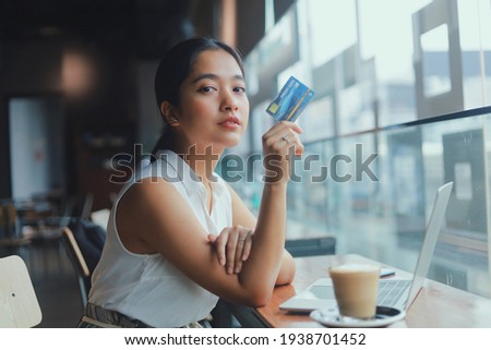 Young woman holding credit card in hand. Beautiful young Asian woman using laptop while sitting in coffee shop