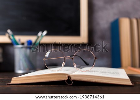 Concept to teacher's day. Pens, pencils, books and glasses on table, against the background of chalkboard. Back to school, copy space.