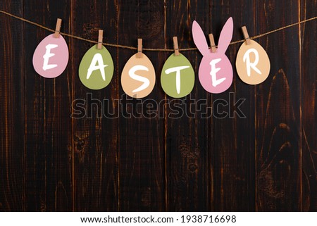 Inscription Easter on colored eggs, on wooden background, a rope with clothespins. The concept of postcards for the Easter holiday.